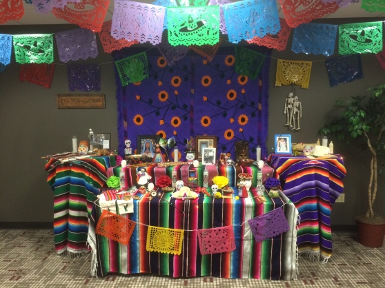 Banners made from different colors of paper that have been cut into shapes of cacti, sombreros and suns hang from the ceiling. Four tables – two rectangular and two circular – are decorated with phots, candles and figurines.